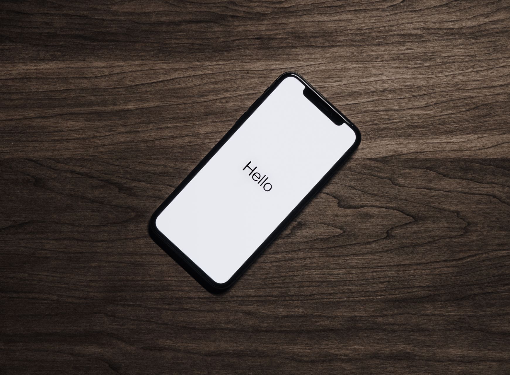 iPhone on dark wood showing the Hello setup screen
