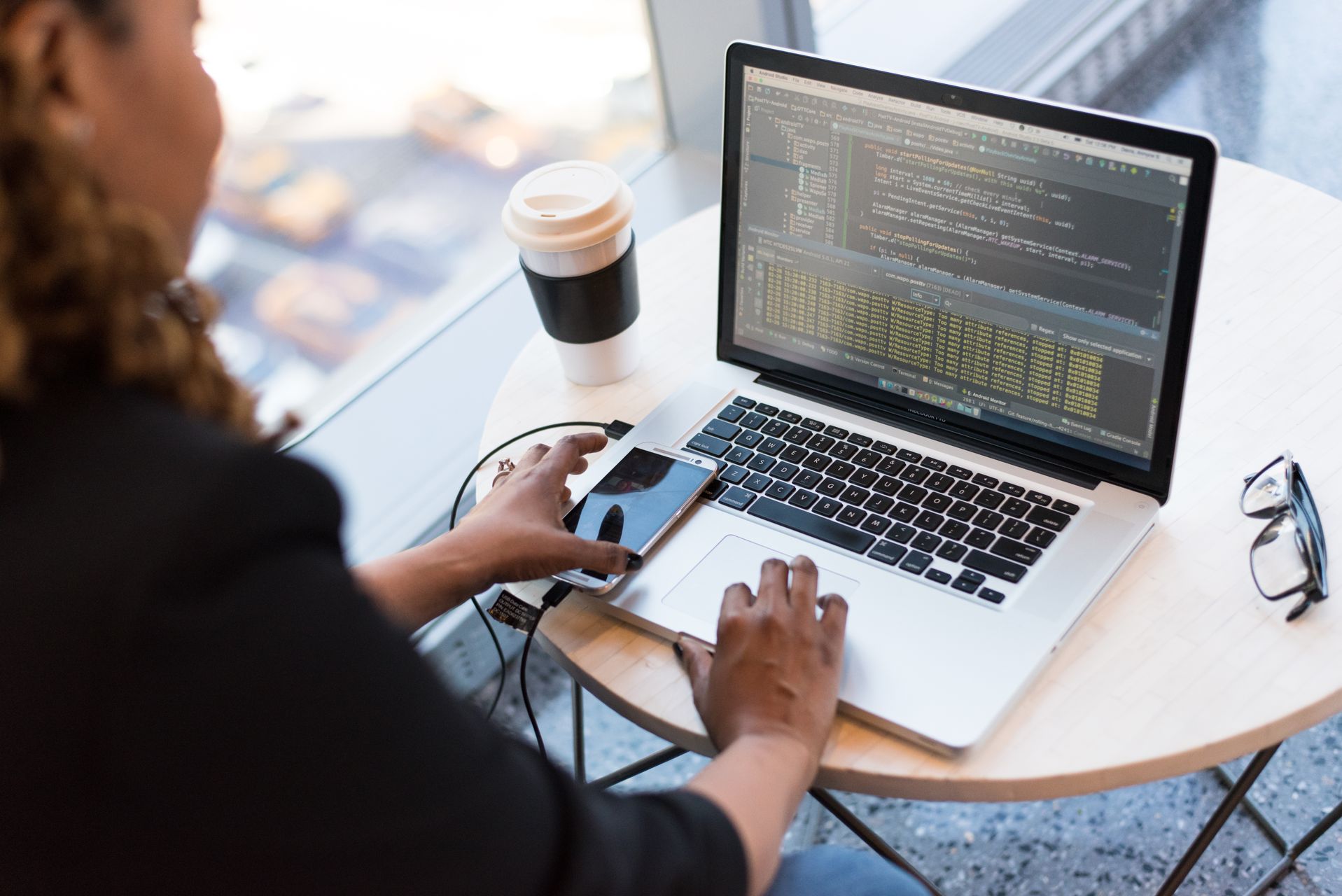 MacBook Pro on a round table showing a code editor with a smartphone connected