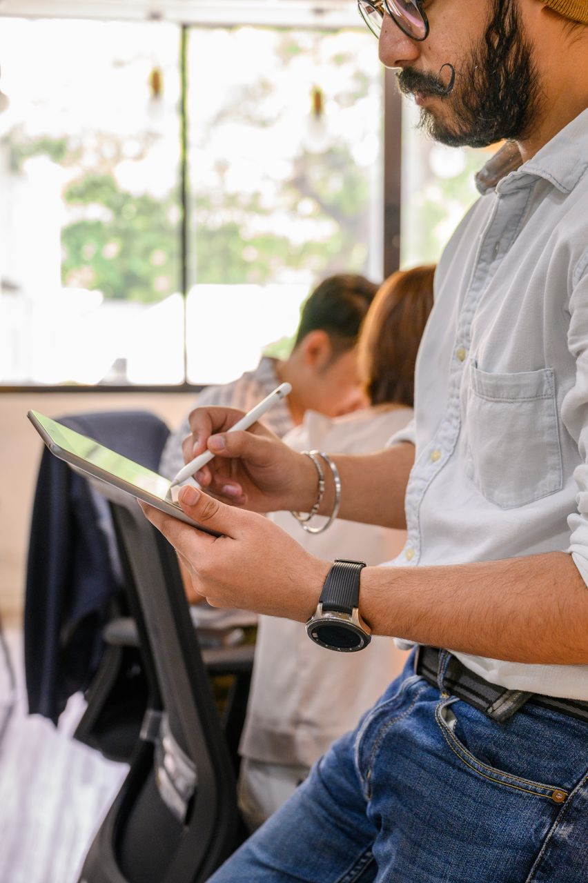 Mann mit Bart schreibt im Büro mit weißem Stift auf einem Tablet