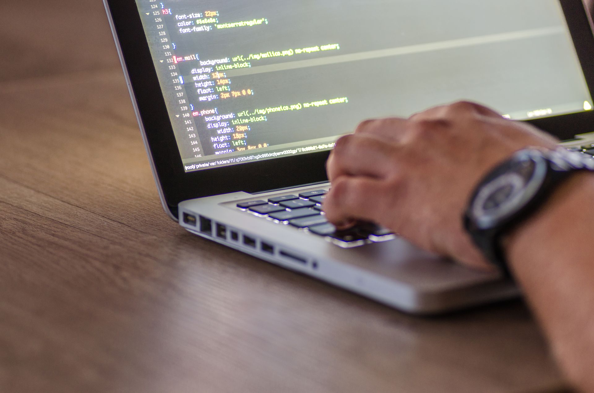 Silver MacBook Pro with CSS code on screen, hand on keyboard