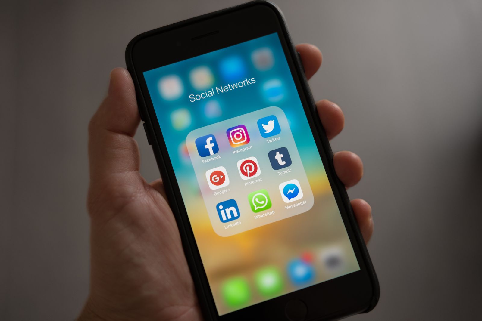 A hand holds a black iPhone whose screen shows a folder titled Social Networks, filled with app icons