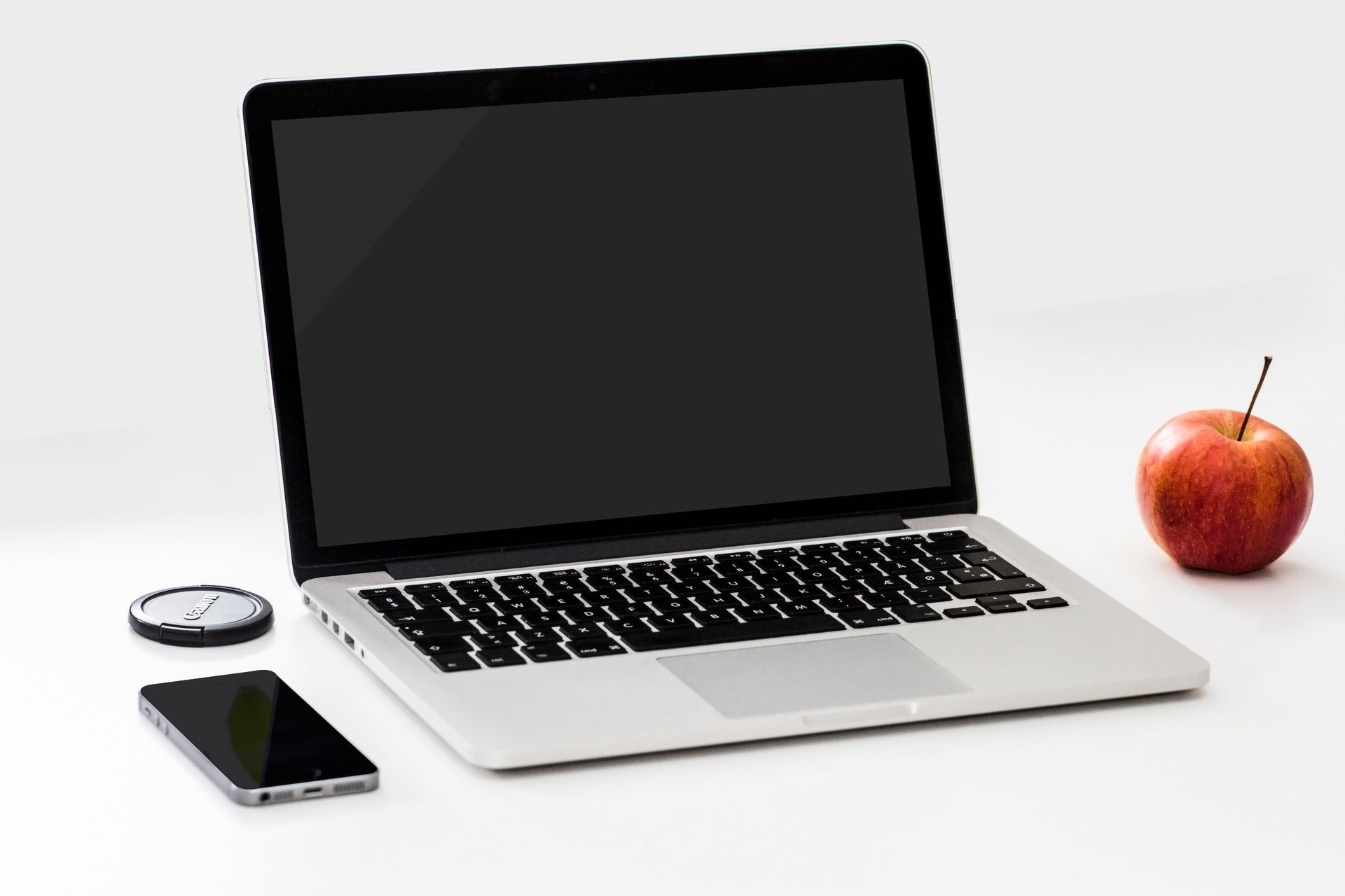 MacBook Pro argenté ouvert sur bureau blanc avec iPhone