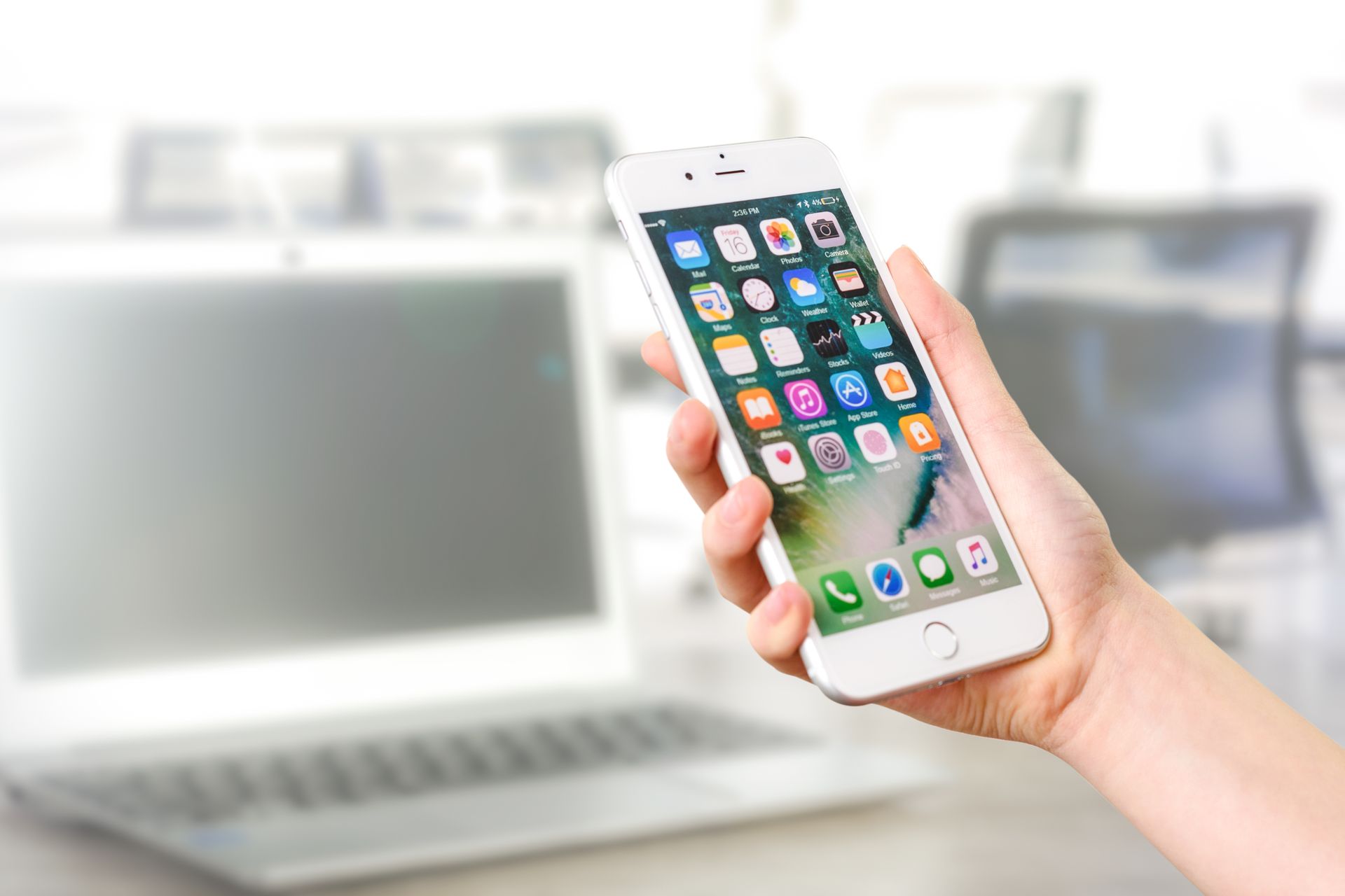 Main tenant un iPhone blanc affichant l'écran d'accueil iOS