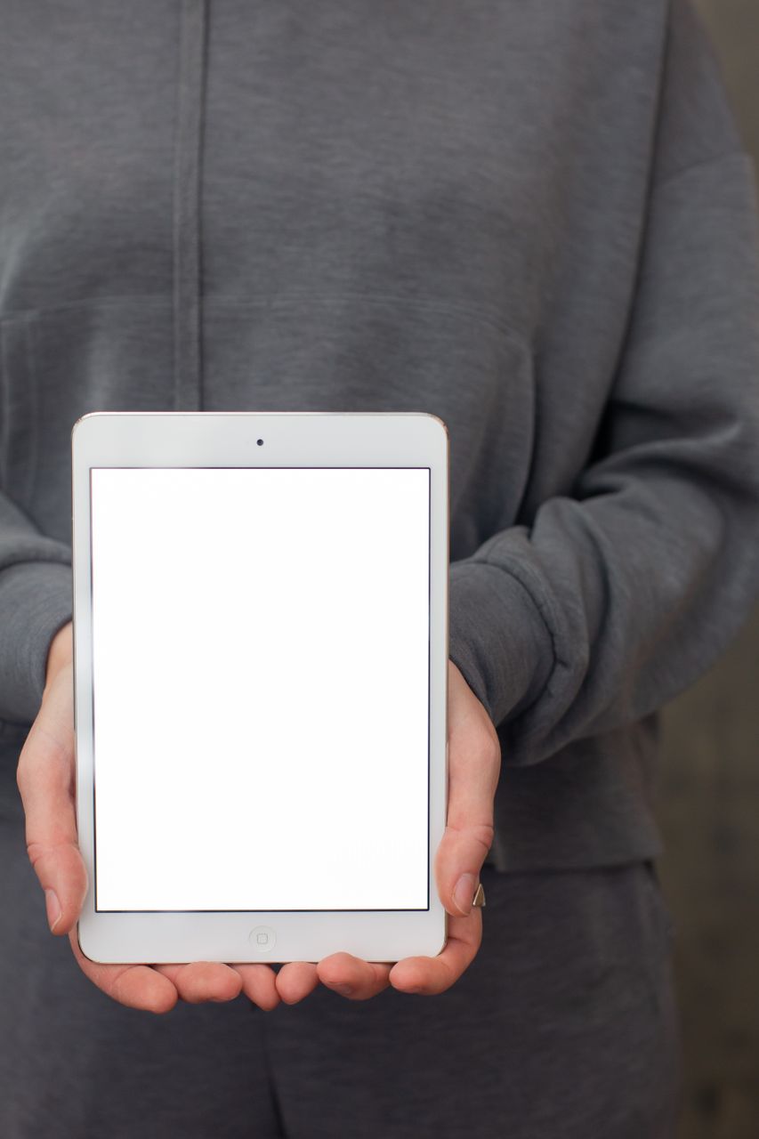 グレーのパーカーを着た人が白い iPad を両手で持ち、画面は真っ白