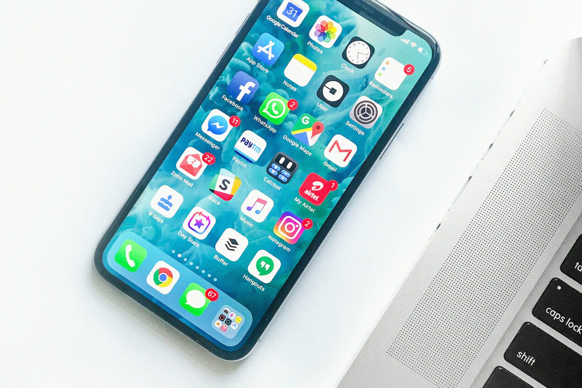 白い机の上の iPhone ホーム画面と MacBook キーボード