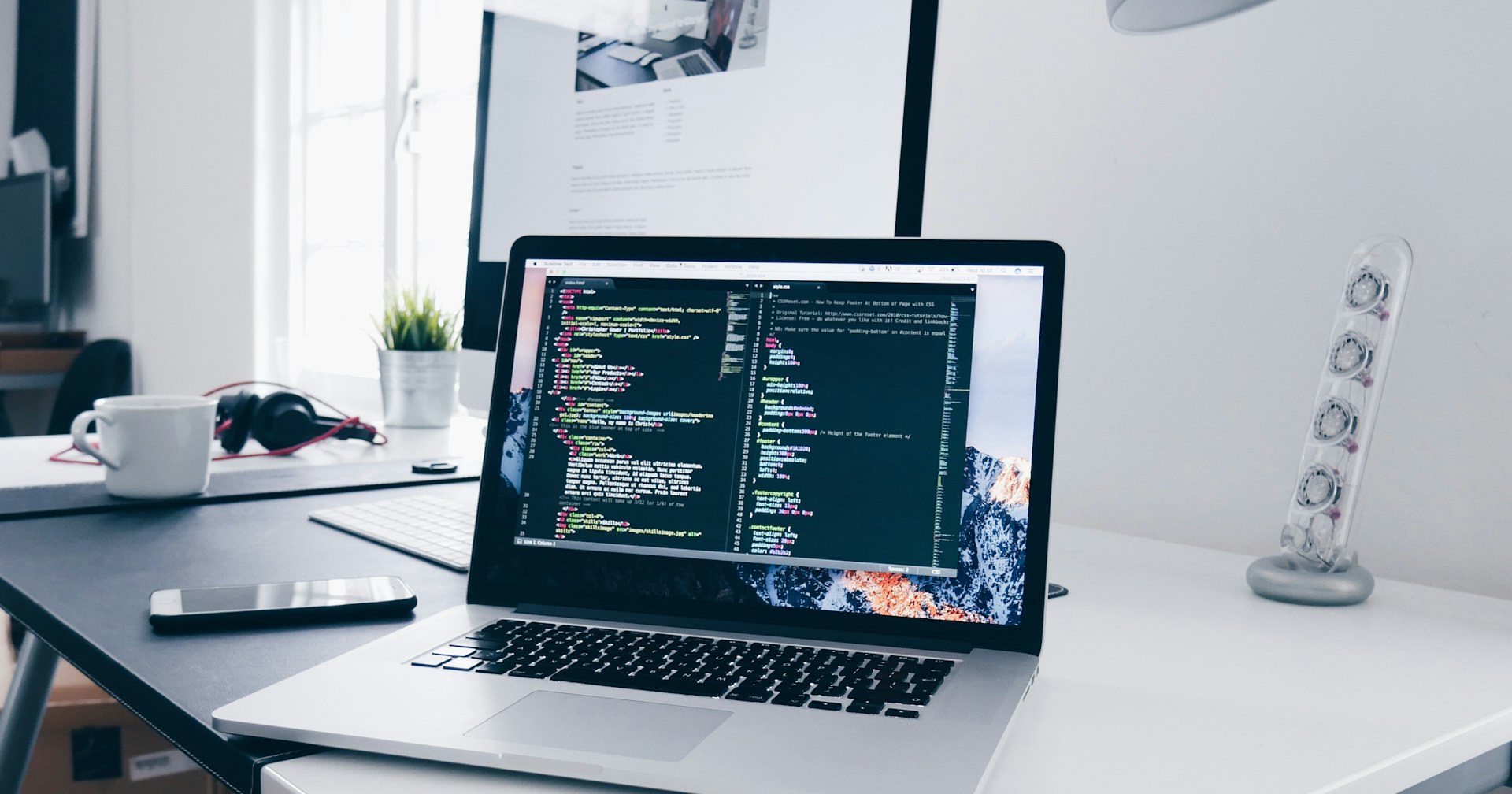 デスク上のノートPC。分割表示のコードエディタに HTML と CSS