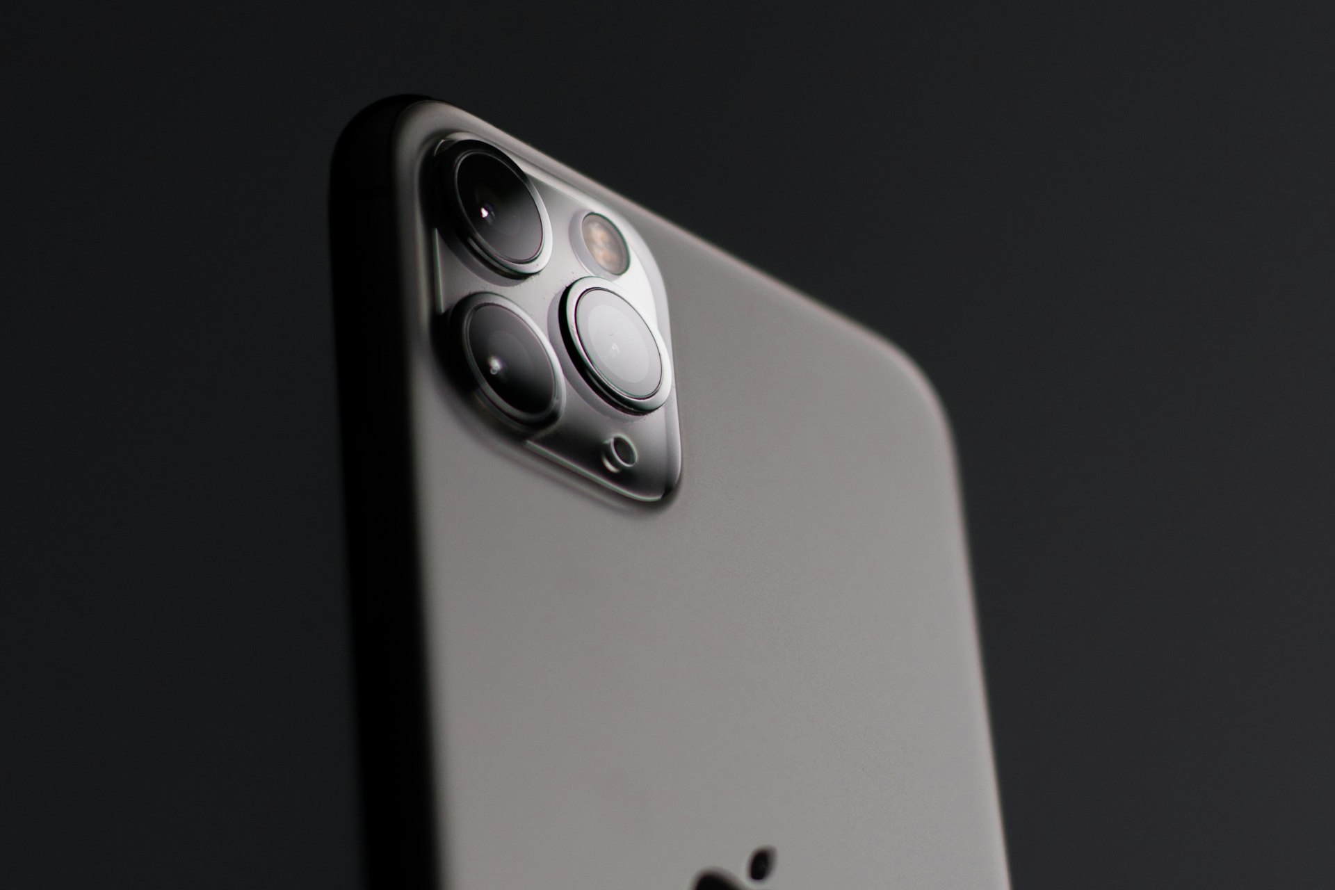 深色 iPhone 三鏡頭模組特寫，底部可見 Apple 標誌