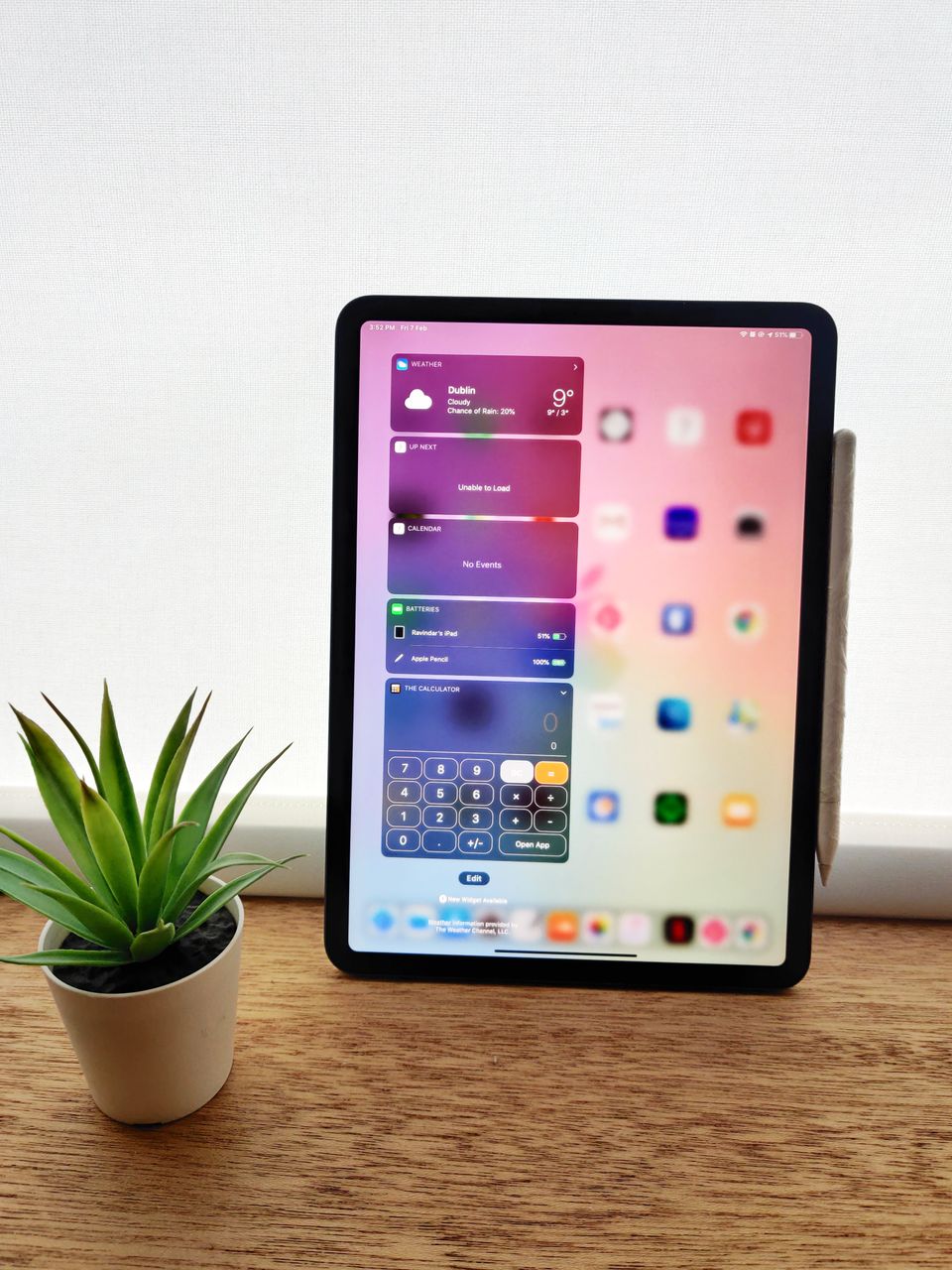 木桌上直立的黑色 iPad，螢幕顯示小工具與計算機，旁有仙人掌與手寫筆
