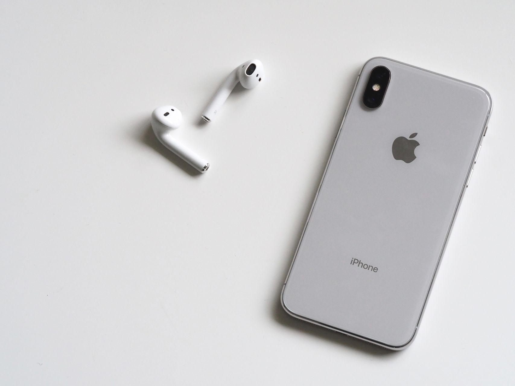 白色 iPhone 与一副白色 AirPods 放在浅色桌面上