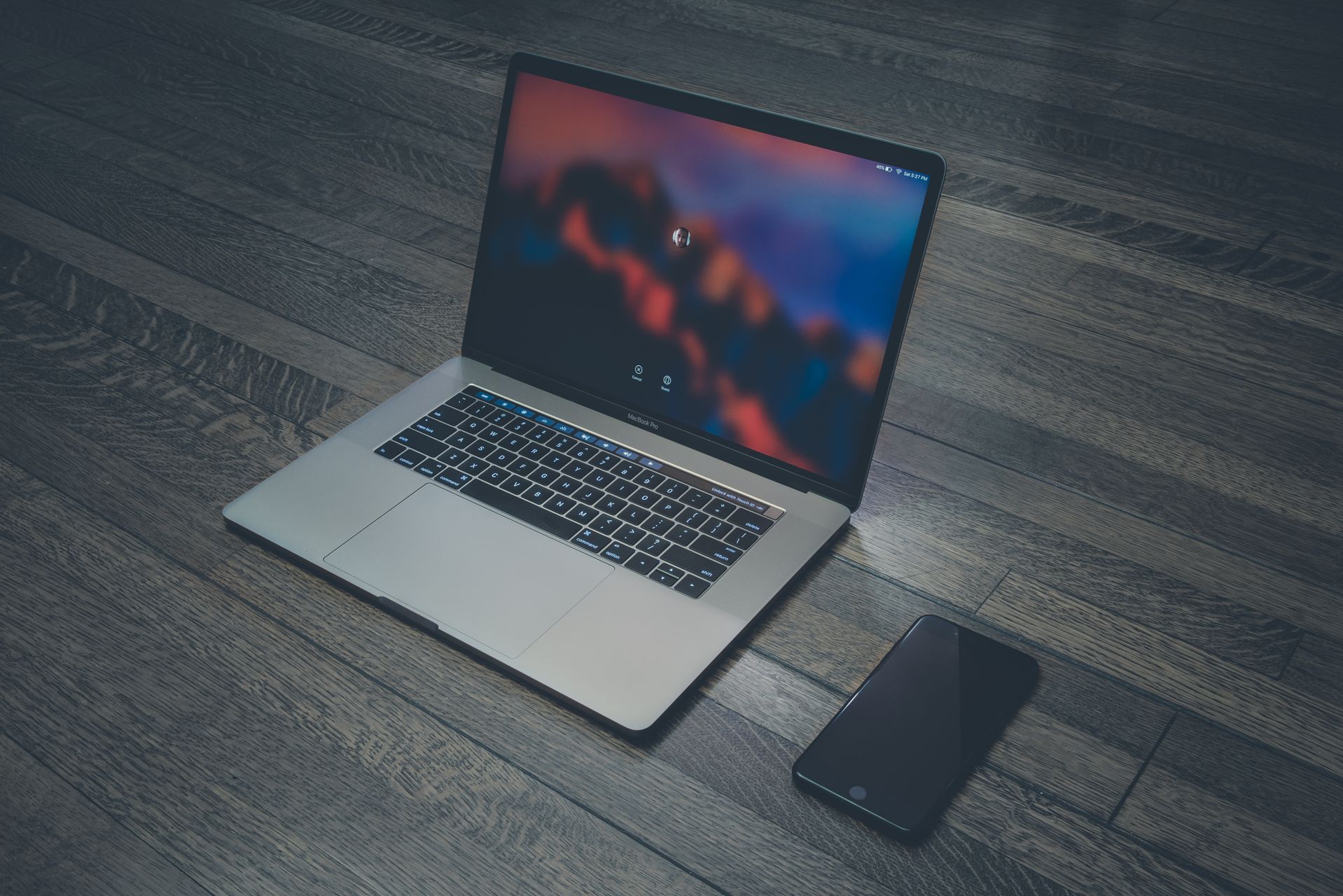 银色 MacBook Pro 打开放在深色木地板上，屏幕显示 macOS 登录界面